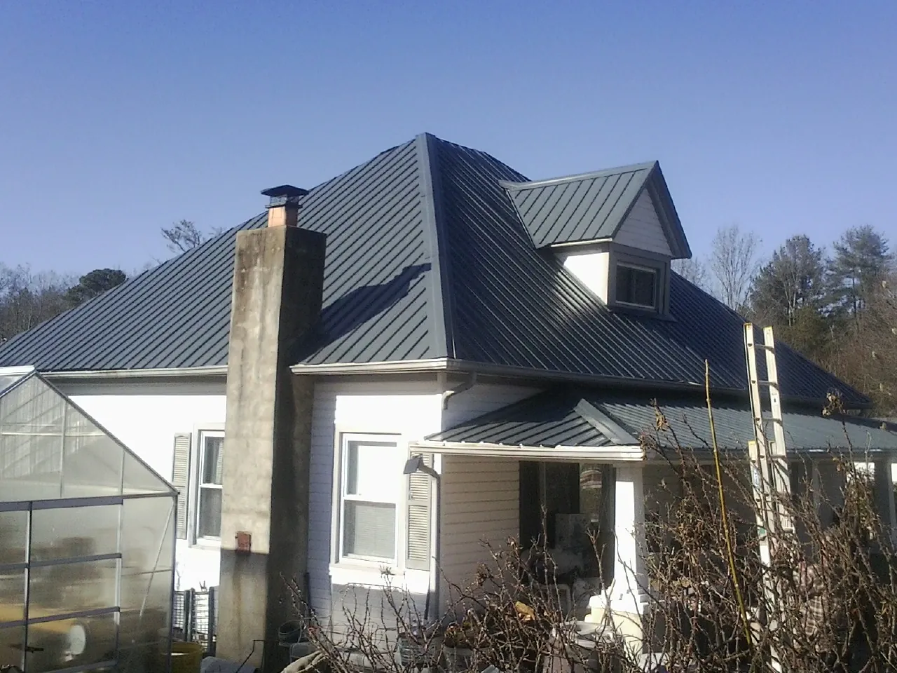 Dark blue standing seam metal roof on a white farmhouse with dormer — Slate & Tile Roof Repair by Roofing Brothers in North Zulch