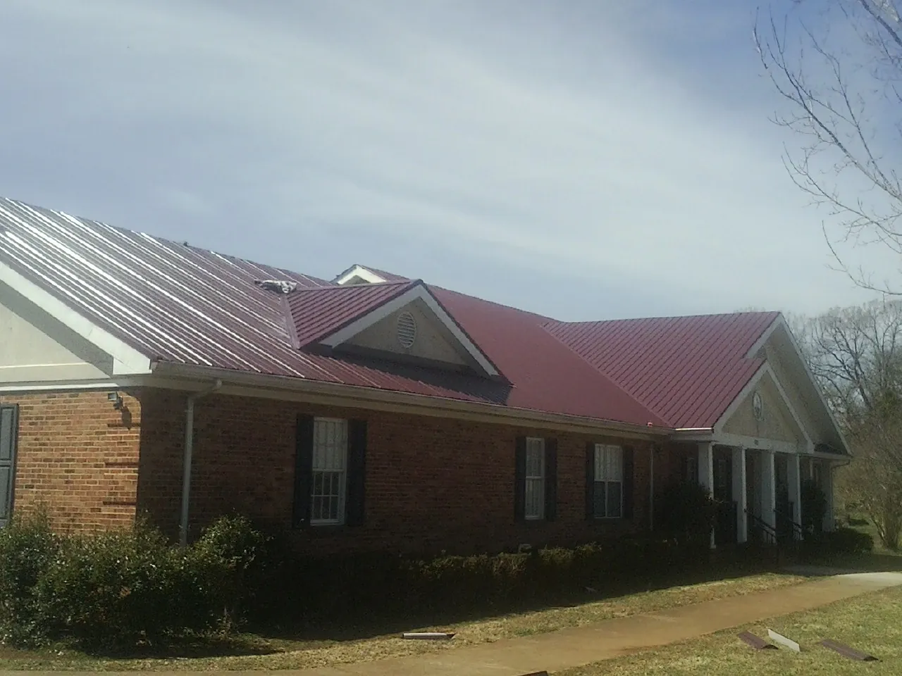 Red metal roof with gabled entries on a long brick building, from a Hail Damage Roof Repair job in North Zulch