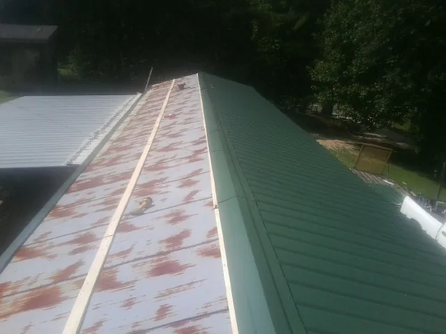 Old rusted panels beside newly installed green metal roofing — Wind Damage Roof Repair by Roofing Brothers in North Zulch