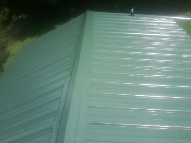 New green metal panels meeting at the ridge of a roof — Flat Roof Repair work by our crew in North Zulch
