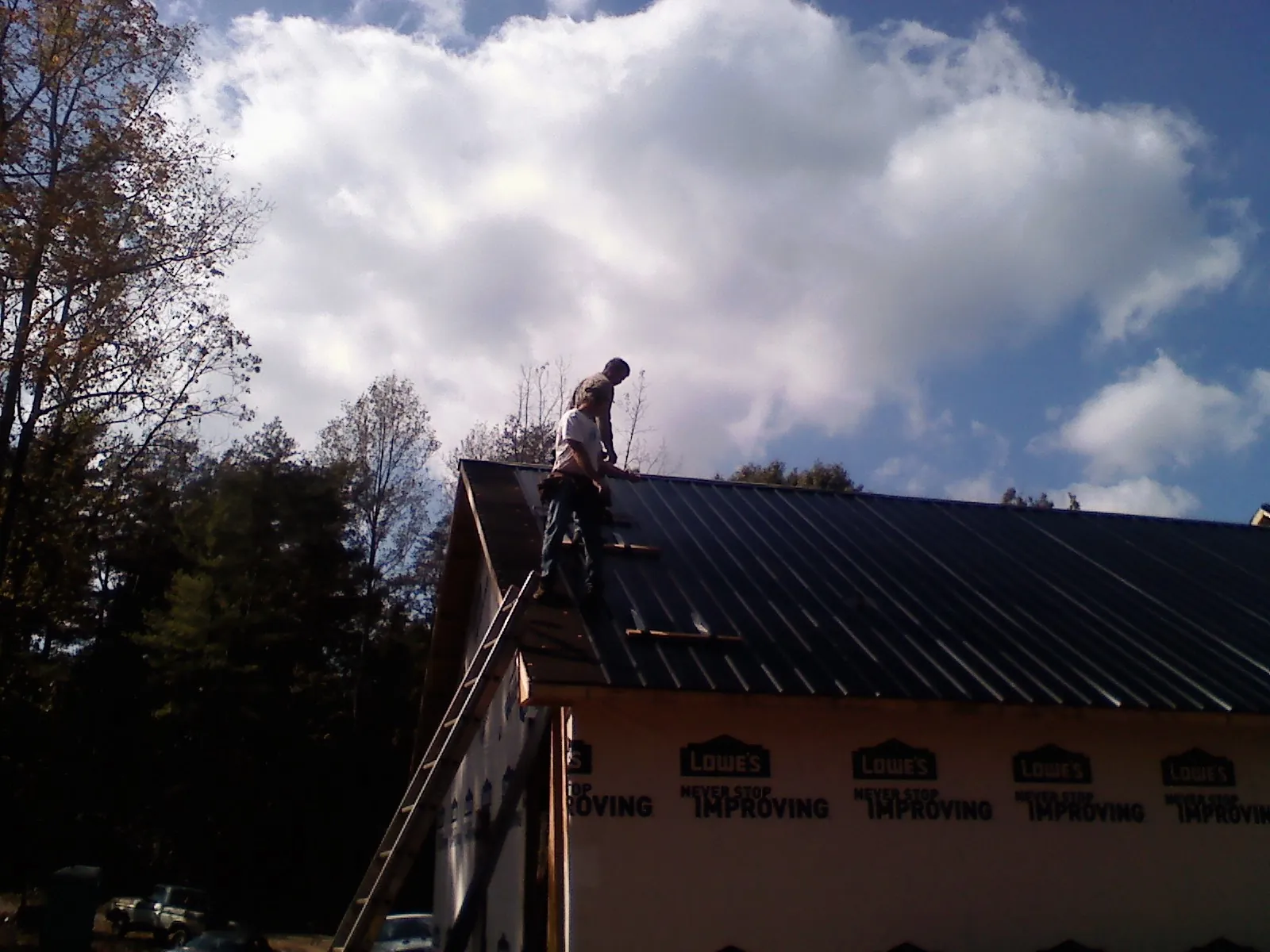 Roofer fastening dark metal panels high against a cloudy sky, from a Roof Inspection job in North Zulch