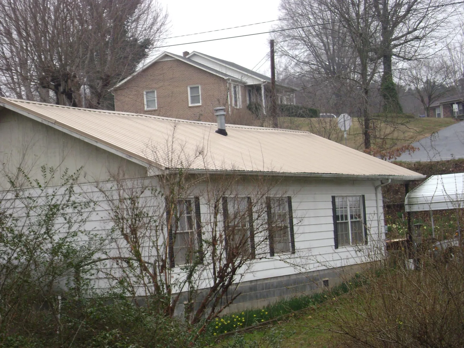 Tan metal roof on a white sided house set into a hillside — Commercial Roofing by Roofing Brothers in North Zulch