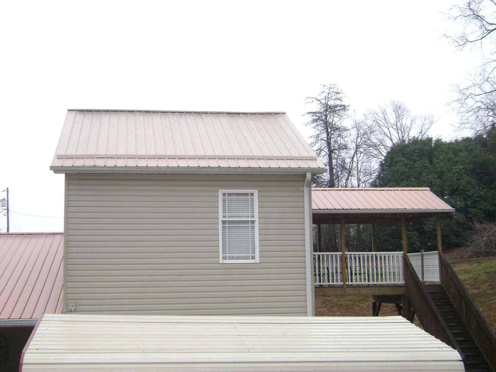 Tan metal roofs on a two story addition and attached porch, from a Roof Replacement job in North Zulch